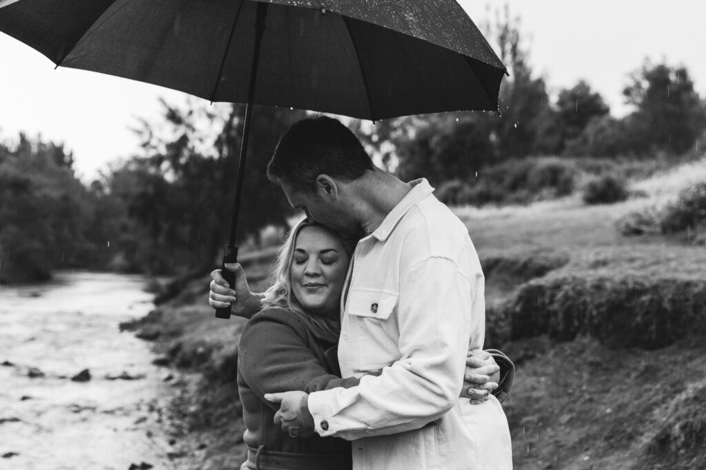 Parents embracing under an umbrella in the rain during a black and white family photoshoot in Gympie.