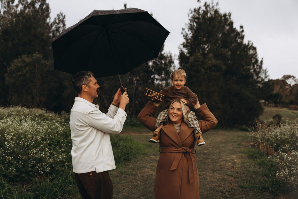 Gympie family photographer. Mother carrying her son on her shoulders while the father holds an umbrella during a Gympie family photography session.