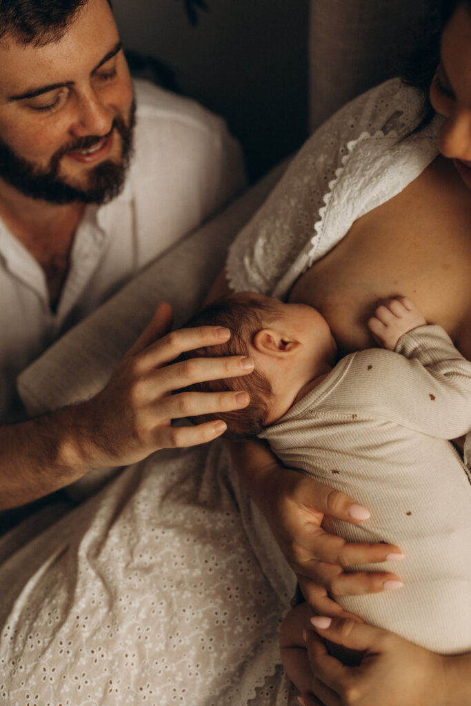 Father gently holding newborn’s head while baby breastfeeds – newborn family photography Gympie